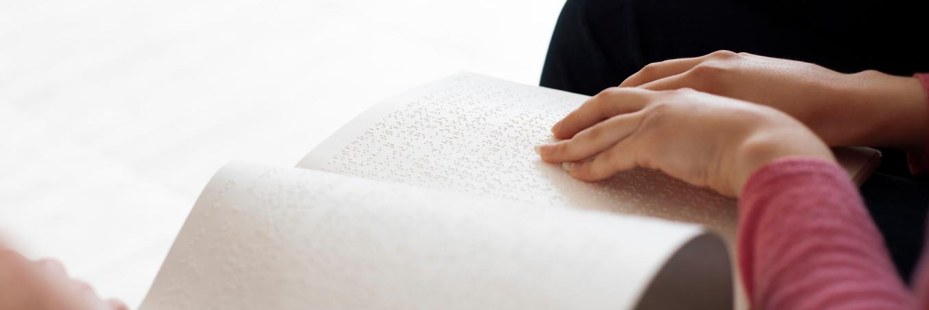 Hands read white paper with Braille text.